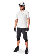 MTB rider wearing Alpinestars A-Aria Astar Short Sleeve Jersey in White Dove, paired with black mountain bike shorts, white helmet, and black knee guards, featuring a small black logo on the chest, coordinated cycling gear for trail performance
