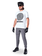 Alpinestars A-Dura Oscar Jersey - Short Sleeve, White Dove with large black spiral graphic, worn by a rider with grey MTB pants, black helmet, and gloves, performance cycling apparel for off-road riding