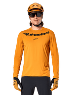 Alpinestars A-Dura Rocker Long Sleeve Jersey in Dark Gold, featuring a black wordmark logo on the chest, worn with a matching gold helmet and gloves for mountain bike performance.
