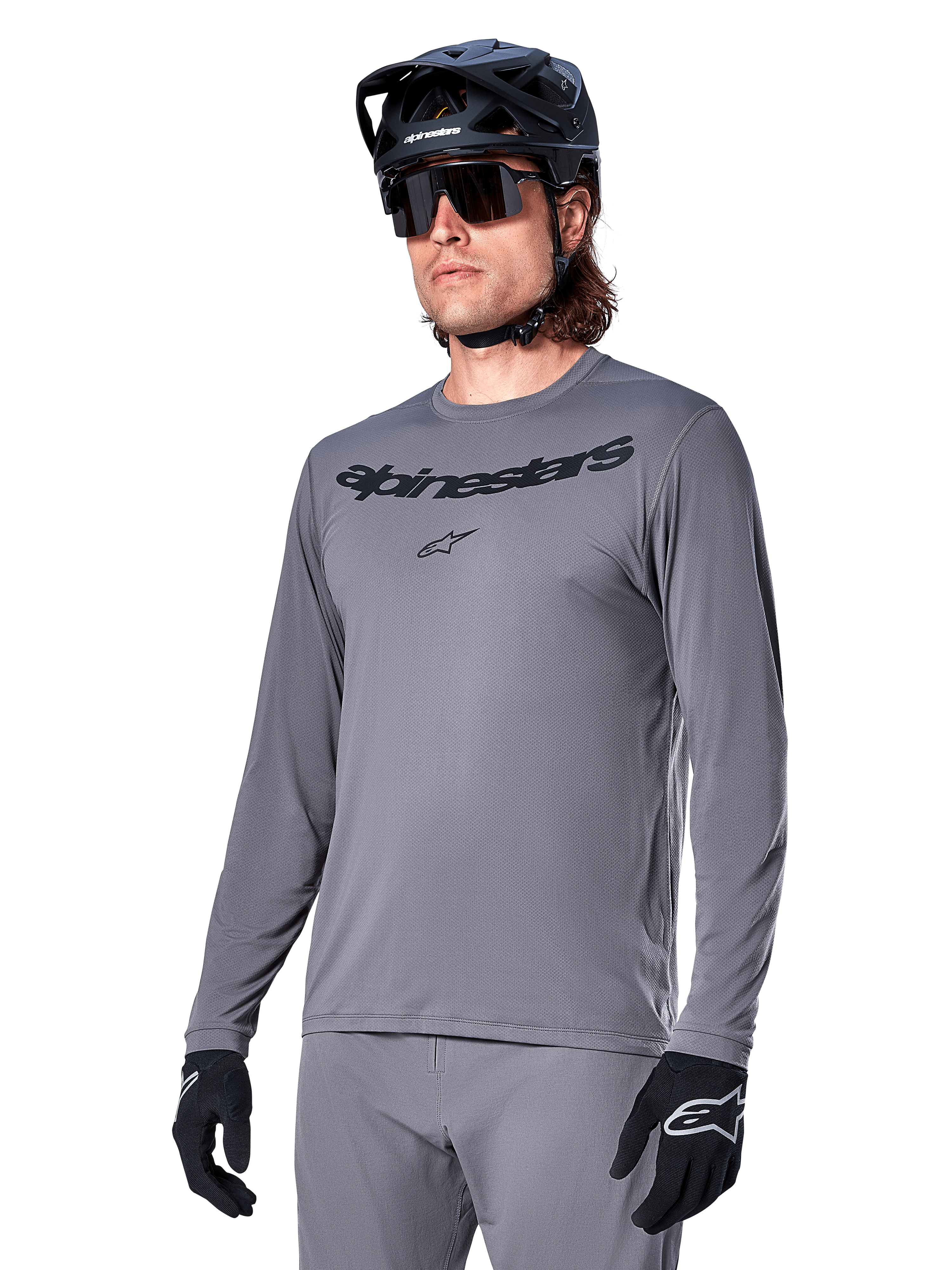 Alpinestars A-Dura Rocker Long Sleeve Jersey, Gray MTB Mountain Biking Jersey, worn with black helmet and gloves, featuring black wordmark on the chest, sporty cycling apparel for off-road riding, plain background