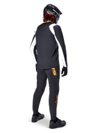 Alpinestars A-Supra Oscar Long Sleeve Jersey, Black with white panels on sleeves, worn by an MTB rider from the back with a black full-face helmet and black pants featuring orange logos, cycling apparel for off-road gravity riding