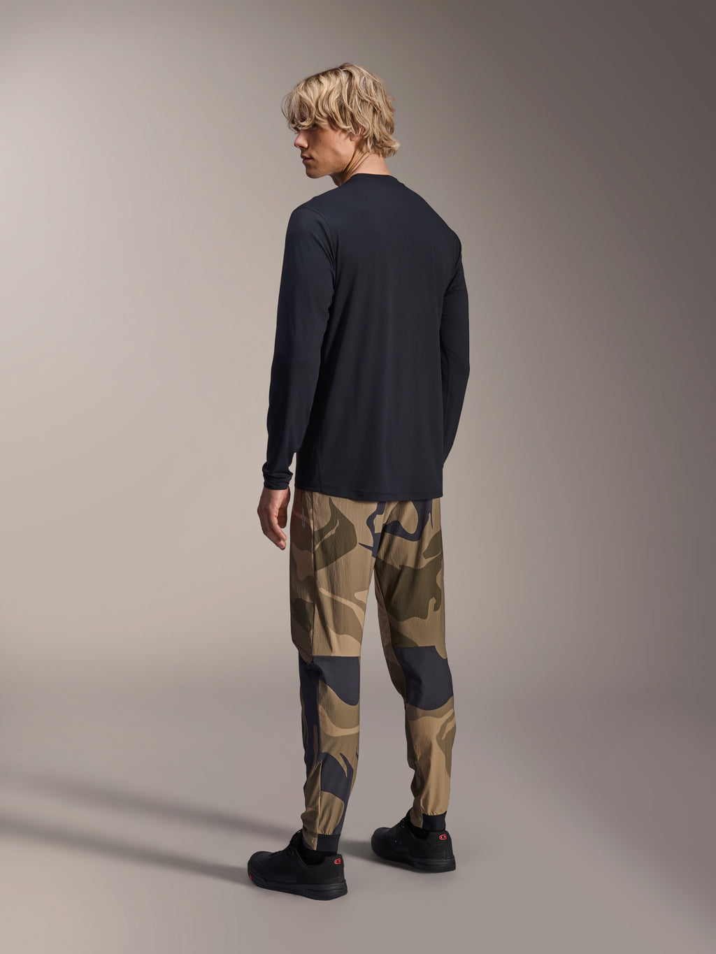 Alpinestars A-Dura Astar Long Sleeve Jersey, Black, back view on a model, paired with camouflage pants, casual MTB performance gear with a drop tail hem and regular fit