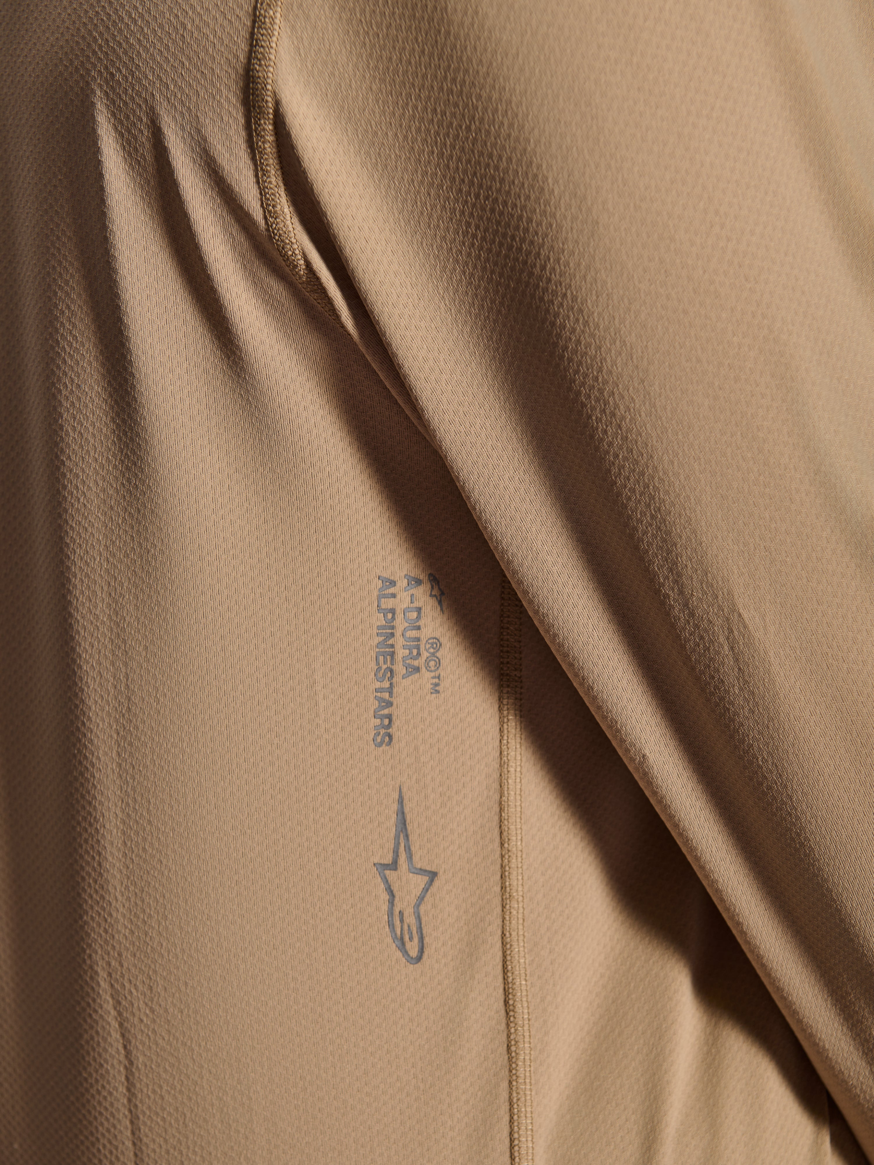 Alpinestars A-Dura Astar Langarmtrikot, MTB-Radtrikot, Braun, Nahaufnahme der Jacquard-Gewebetextur, aufgedrucktes Astars-Logo und A-Dura-Schriftzug, technische Mountainbike-Bekleidung