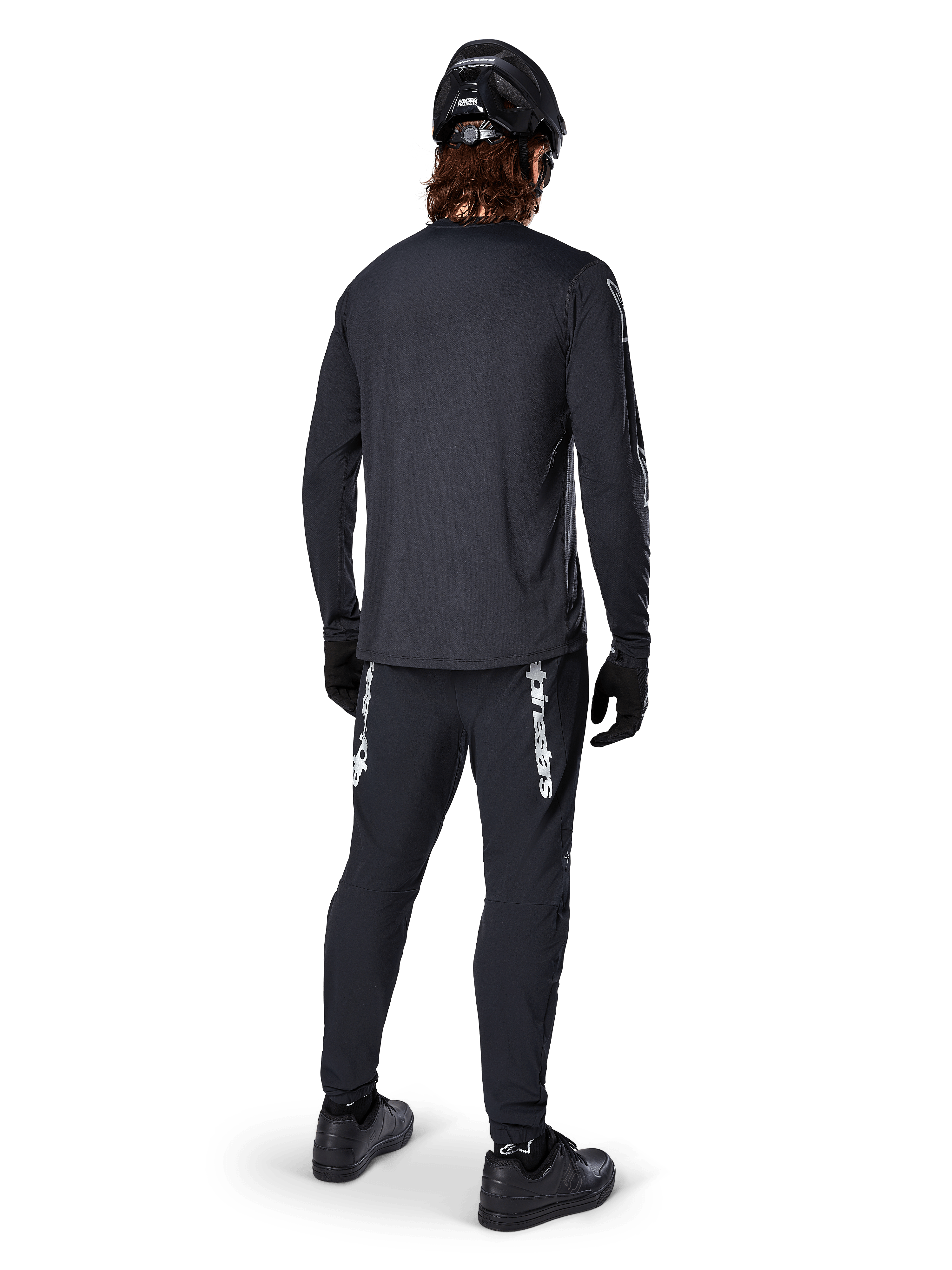 Alpinestars A-Dura Switch Long Sleeve Jersey, Black, rear view on a rider, worn with black pants featuring white Alpinestars branding, black helmet, and gloves, featuring a drop tail for extra coverage, performance mountain bike apparel