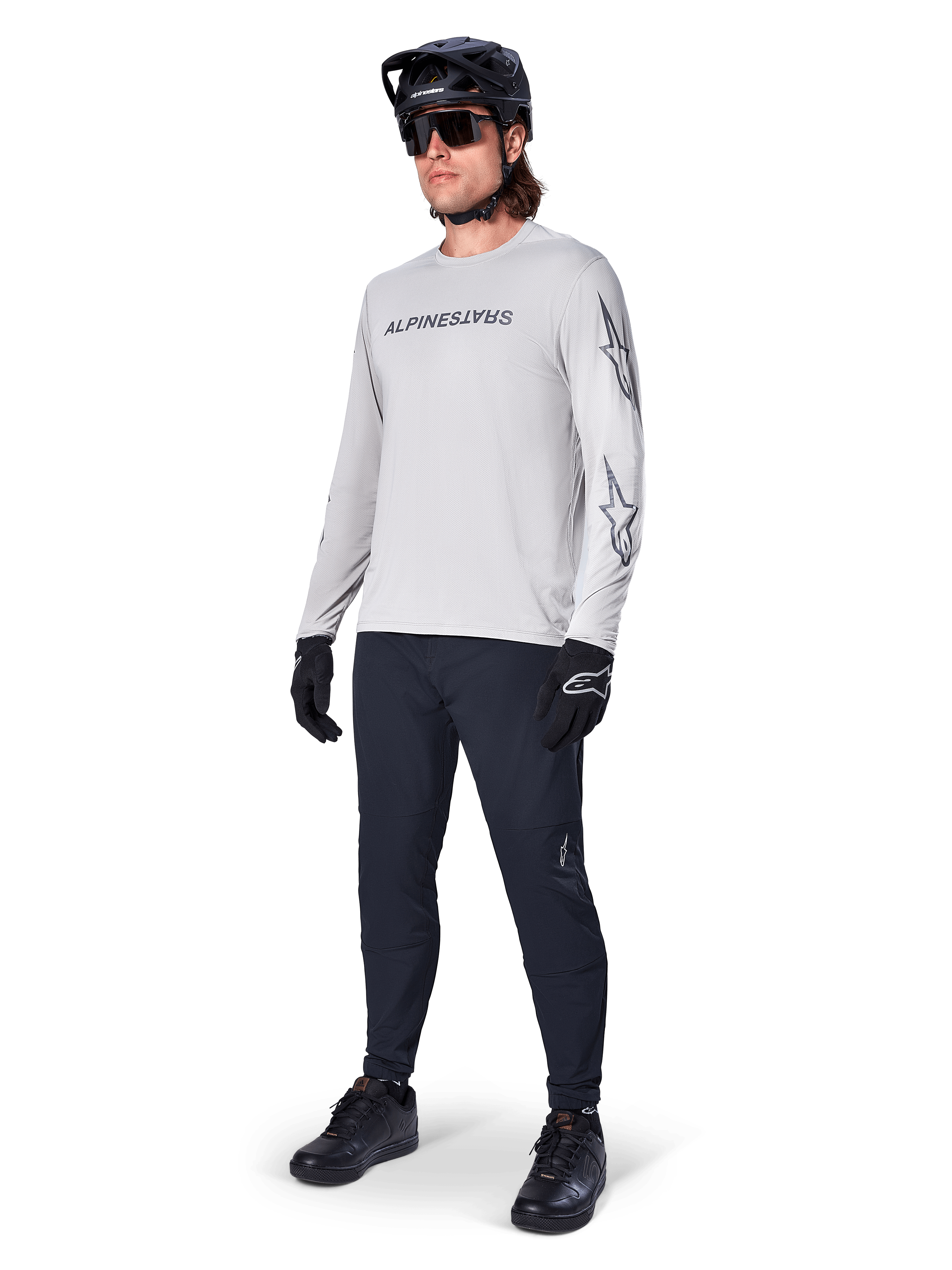 Alpinestars A-Dura Switch Long Sleeve Jersey, Light Gray, worn by male rider with black mountain bike pants and helmet, featuring black wordmark logo on chest and star graphics on sleeves, performance off-road cycling gear
