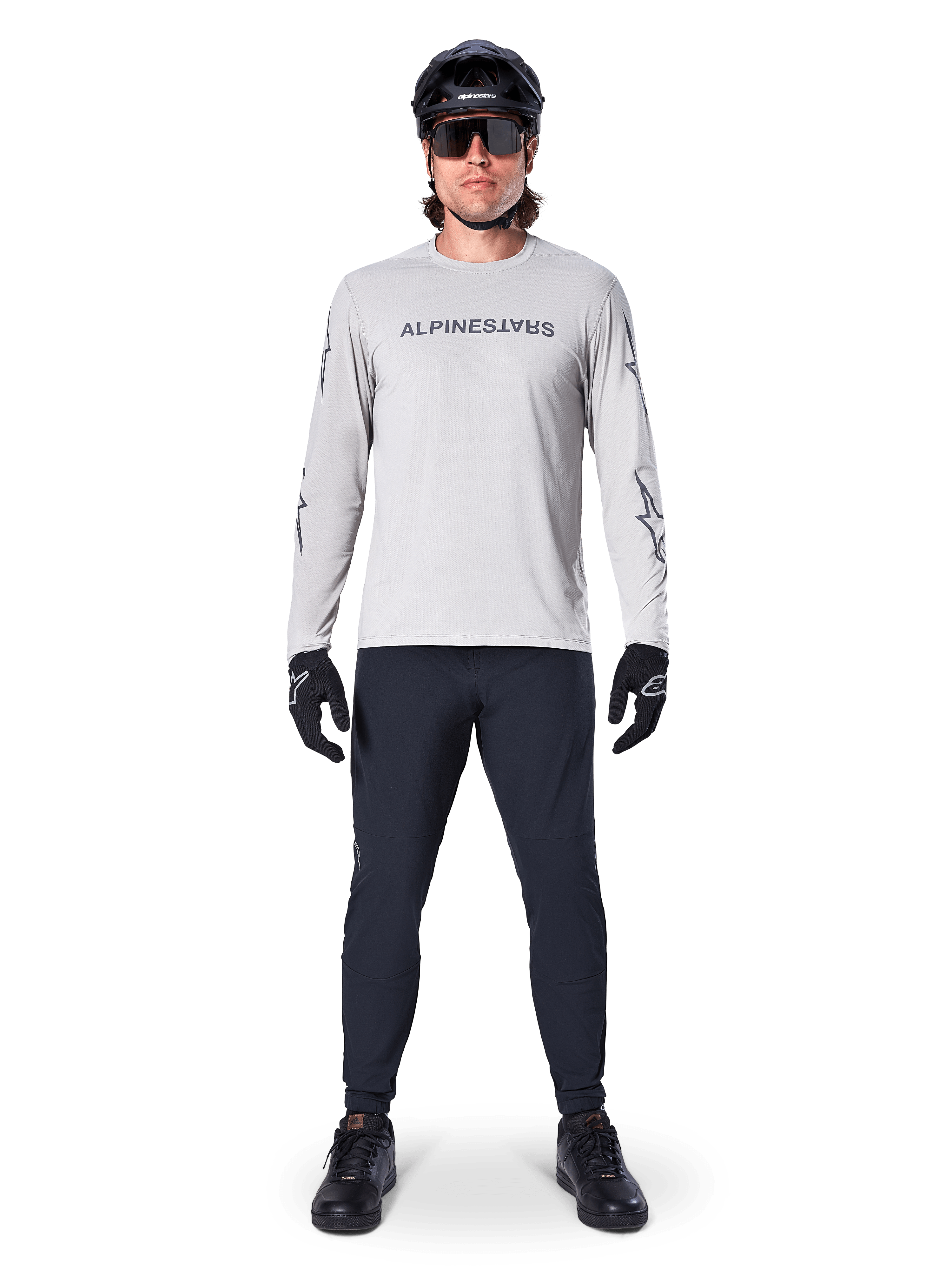 Alpinestars A-Dura Switch Long Sleeve Jersey in Light Gray, featuring a stylized wordmark logo on the chest, worn with black pants, helmet, and gloves, performance mountain bike apparel for off-road cycling