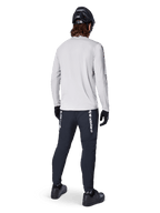 Alpinestars A-Dura Switch Long Sleeve Jersey, Light Gray, rear view on a rider wearing black cycling pants, helmet, and gloves, high-performance mountain bike gear with a longer drop tail.