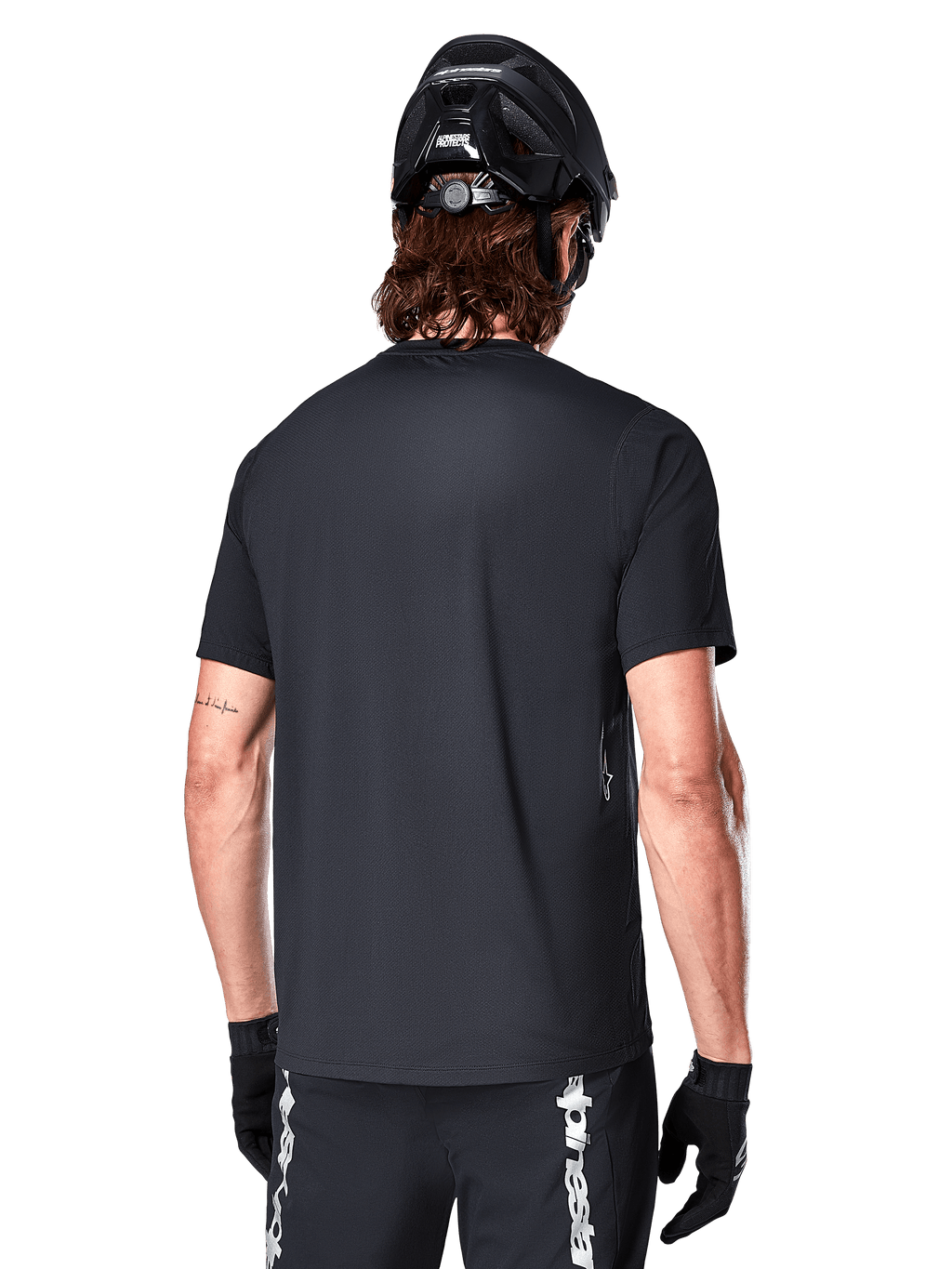 Alpinestars A-Dura Switch Short Sleeve Jersey, Black, rear view on a model wearing a black cycling helmet and MTB shorts, highlighting the regular fit and longer drop tail designed for mountain biking.