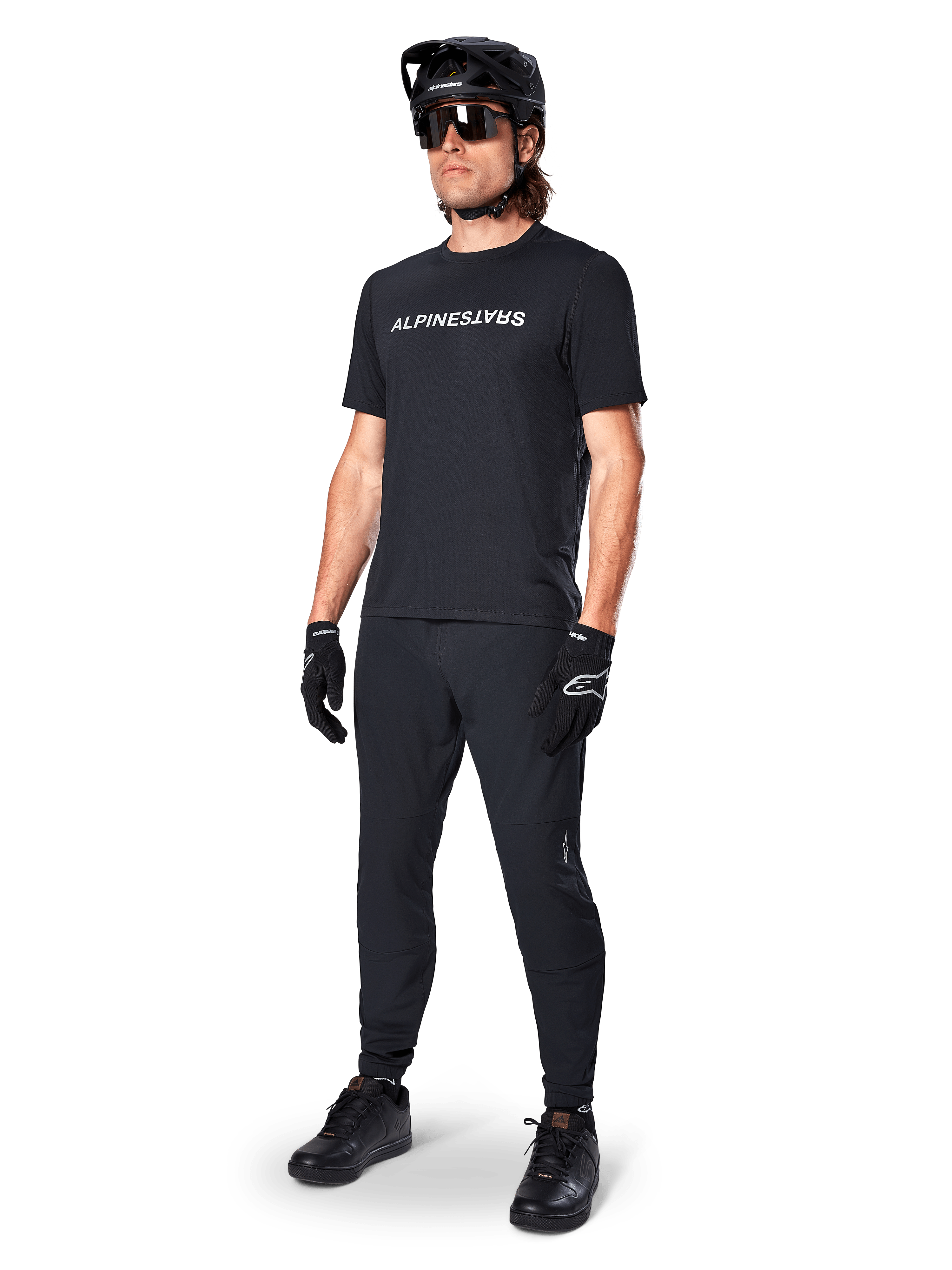 Alpinestars A-Dura Switch Short Sleeve Jersey, Black, worn by model with matching black MTB pants, helmet, and gloves, featuring a white Alpinestars wordmark on the chest, performance mountain bike apparel