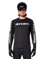 Männlicher Fahrer im Alpinestars A-Dura Dri Oscar Langarmtrikot, Schwarz Reflektierend, mit weißem Alpinestars-Schriftzug auf der Brust und silbernen reflektierenden Grafiken auf den Ärmeln, kombiniert mit schwarzem MTB-Helm, Sonnenbrille und schwarzen Handschuhen, Performance-Radsportbekleidung