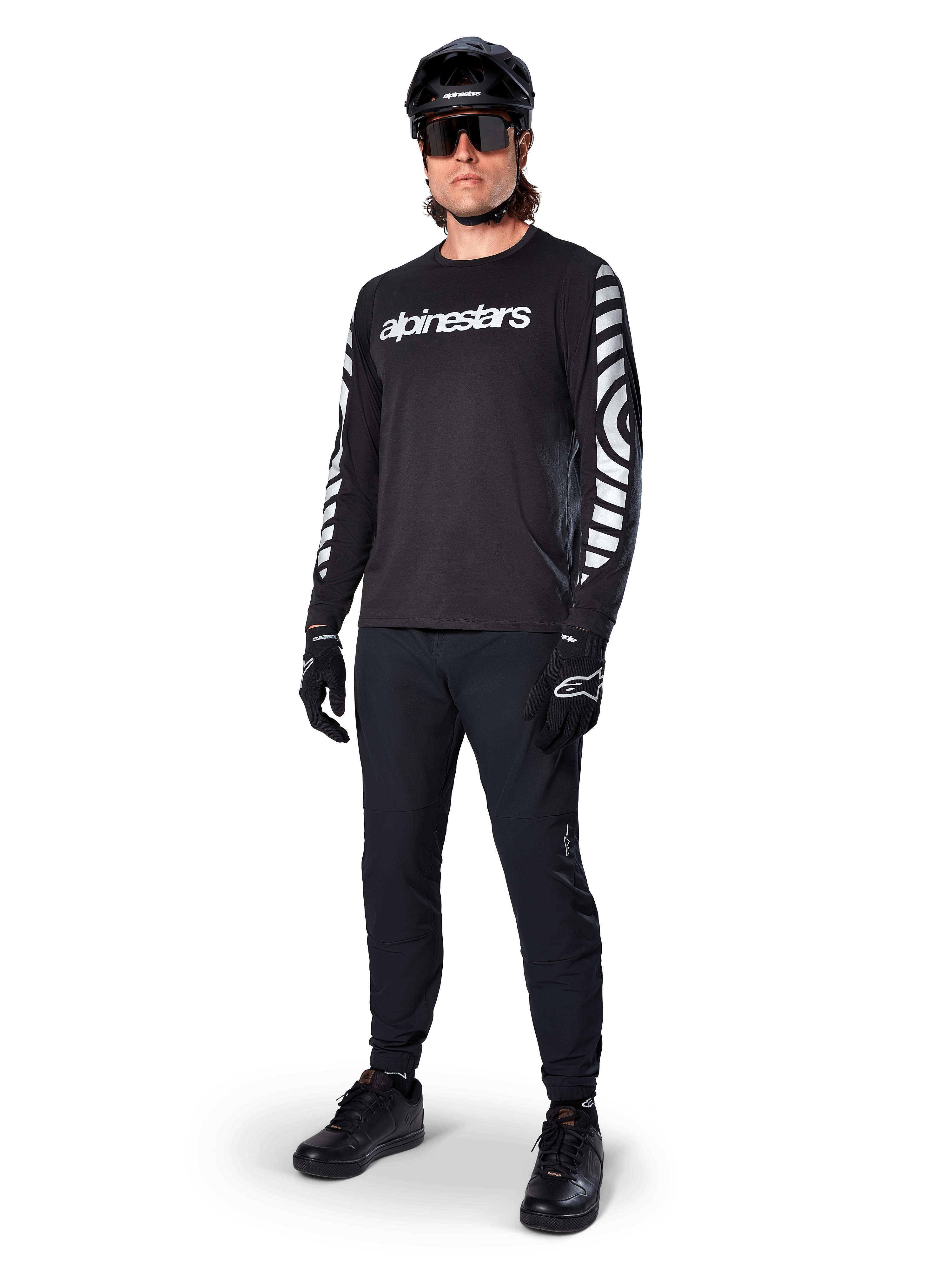 Alpinestars A-Dura Dri Oscar Langarmtrikot, Black Reflective, mit auffälligem weißem Alpinestars-Schriftzug auf der Brust und reflektierenden Grafikmustern auf den Ärmeln, kombiniert mit schwarzer Mountainbike-Hose, Helm und Handschuhen, technische MTB-Bekleidung