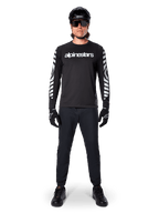 Alpinestars A-Dura Dri Oscar Langarmtrikot in Black Reflective, getragen mit schwarzem Helm und Sonnenbrille, mit weißem Brustlogo und reflektierenden Grafikmustern an den Ärmeln, MTB-Ausrüstung für Offroad-Fahrten