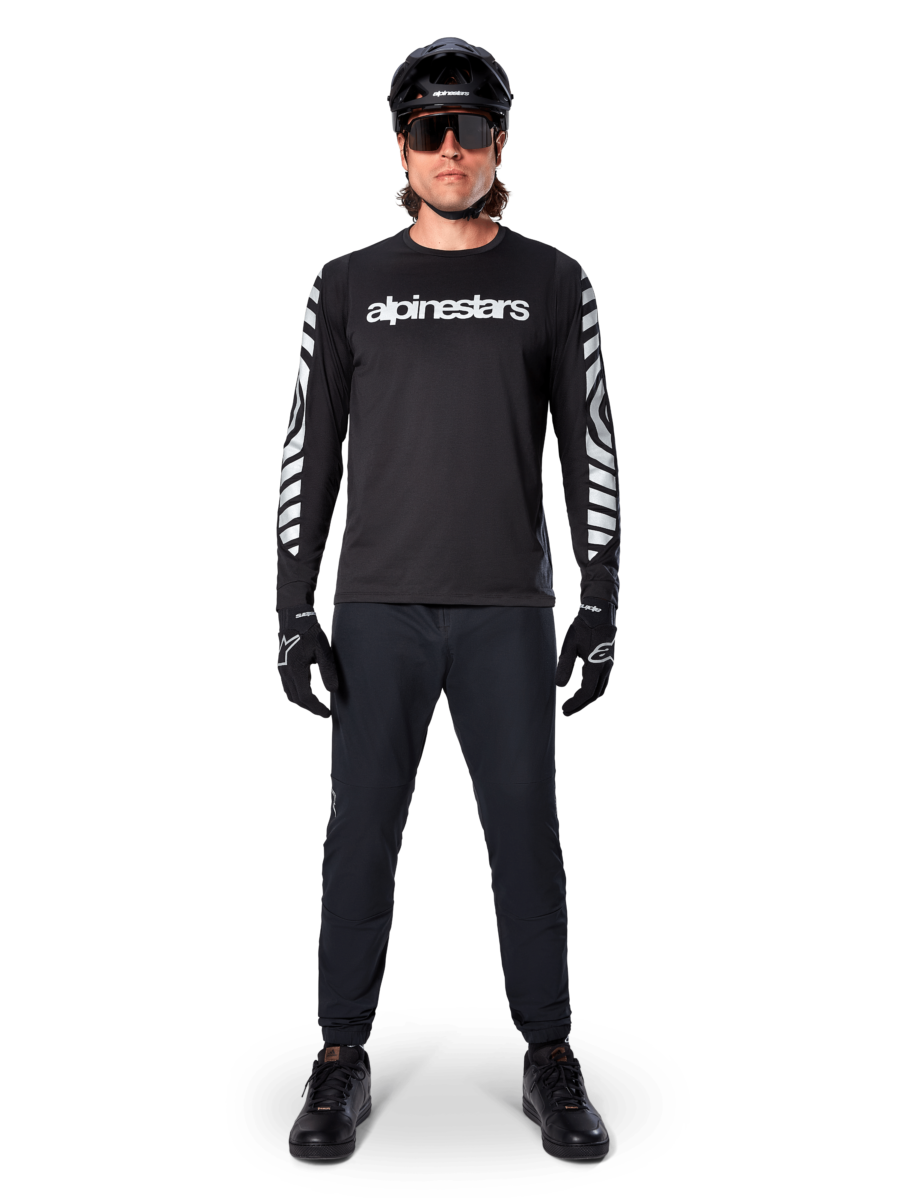 Alpinestars A-Dura Dri Oscar Langarmtrikot in Black Reflective, getragen mit schwarzem Helm und Sonnenbrille, mit weißem Brustlogo und reflektierenden Grafikmustern an den Ärmeln, MTB-Ausrüstung für Offroad-Fahrten