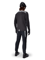 Mountainbike-Fahrer im Alpinestars A-Dura Dri Oscar Langarmtrikot in Black Reflective, Rückansicht, kombiniert mit schwarzer technischer Hose, Helm und Handschuhen, mit reflektierenden Streifengrafiken auf den Schultern und einem verlängerten Rücken für den Offroad-Radsport.