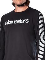 Alpinestars A-Dura Dri Oscar Langarmtrikot, Black Reflective, Nahaufnahme mit weißem Alpinestars-Logo auf der Brust und reflektierenden kreisförmigen Grafiken auf den Ärmeln, technische Radsportbekleidung für Mountainbiking