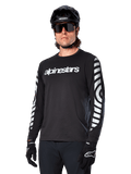 Alpinestars A-Dura Dri Oscar Langarmtrikot, MTB-Fahrradtrikot, Schwarz reflektierend, mit weißem Brust-Schriftzug und markanten reflektierenden kreisförmigen Grafiken auf den Ärmeln, getragen mit schwarzem Helm und Sonnenbrille, technische feuchtigkeitsableitende Bekleidung für Mountainbiking im Gelände