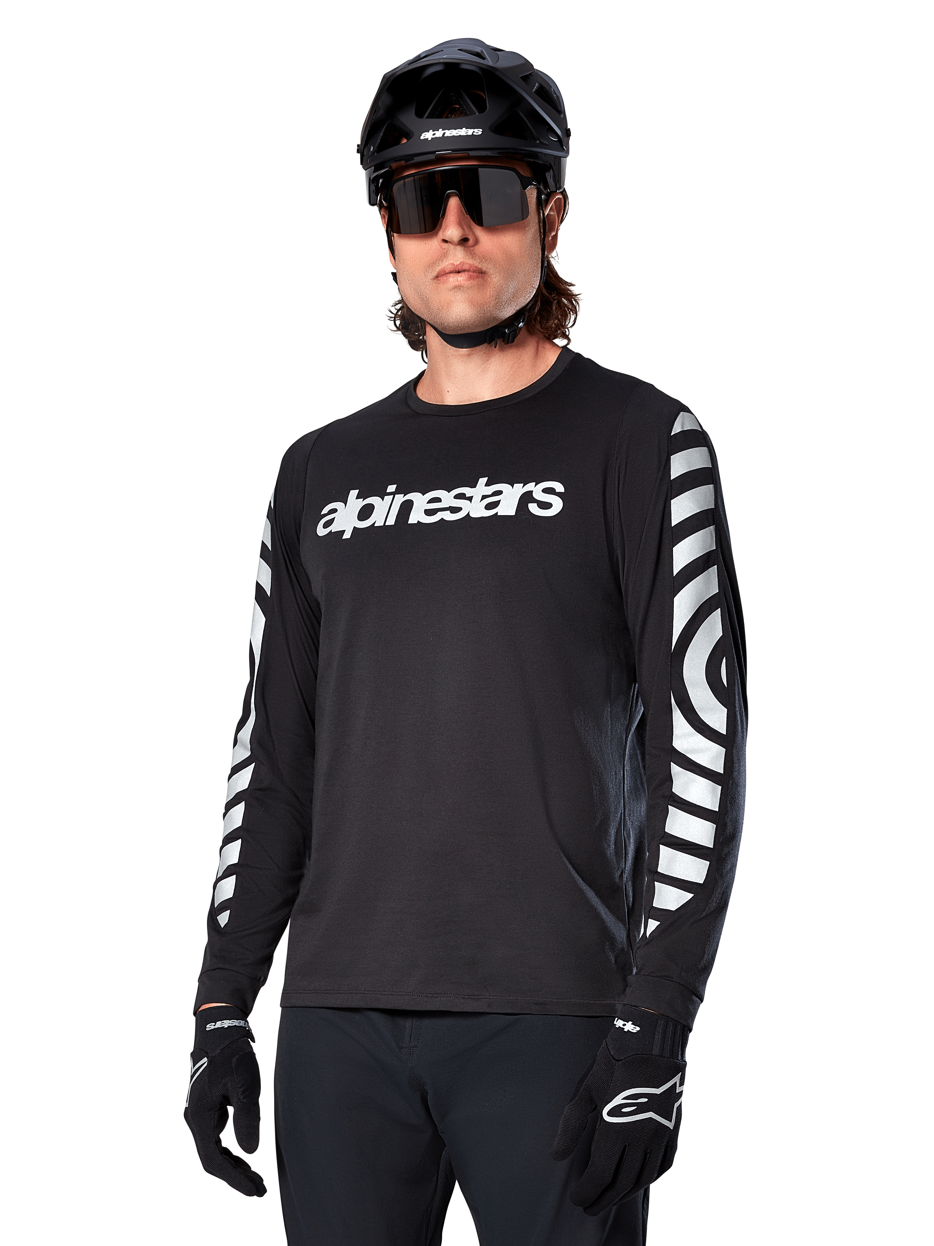 Alpinestars A-Dura Dri Oscar Langarmtrikot, MTB-Fahrradtrikot, Schwarz reflektierend, mit weißem Brust-Schriftzug und markanten reflektierenden kreisförmigen Grafiken auf den Ärmeln, getragen mit schwarzem Helm und Sonnenbrille, technische feuchtigkeitsableitende Bekleidung für Mountainbiking im Gelände