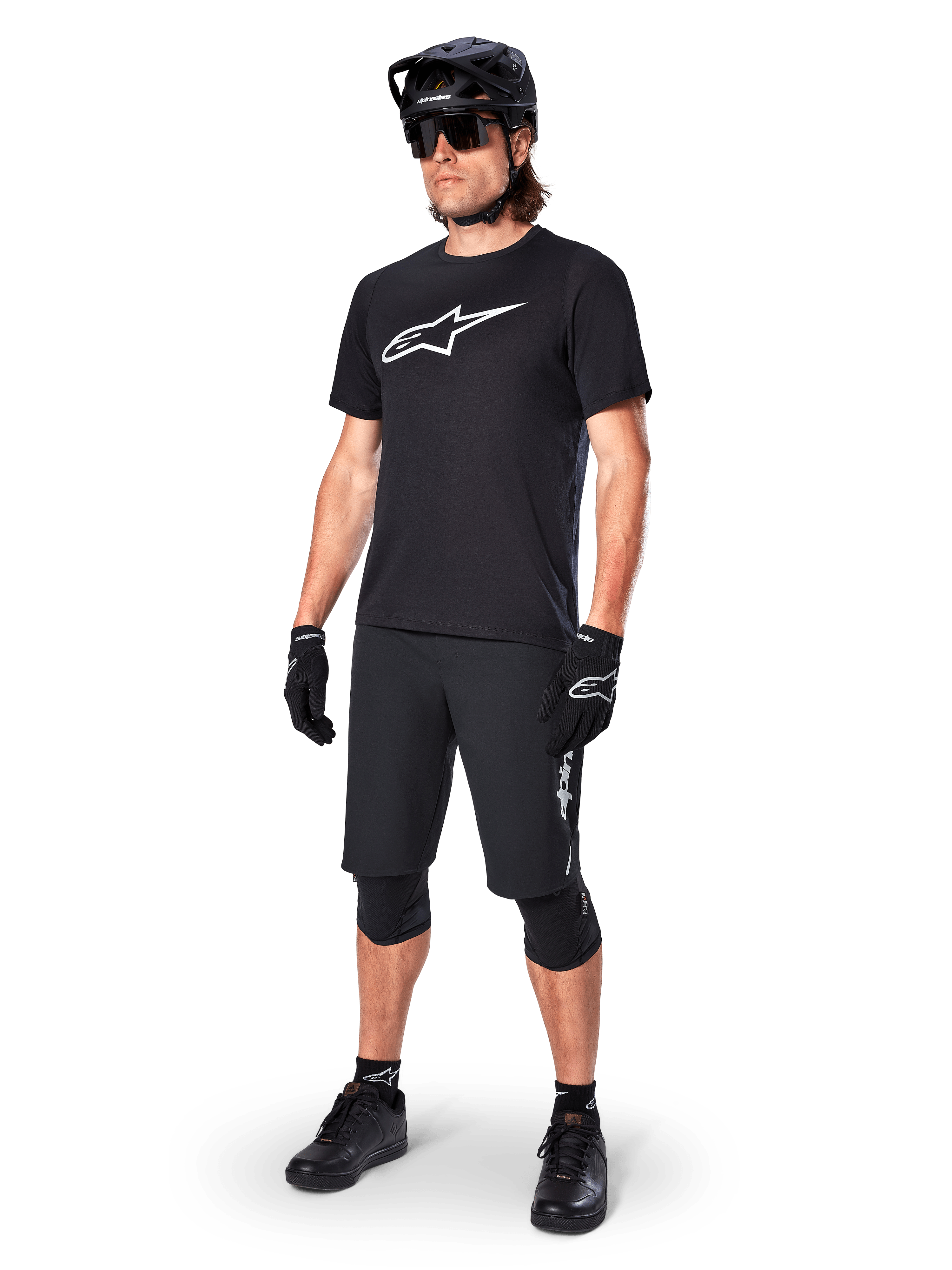 Mountainbike-Fahrer im Alpinestars A-Dura Dri Oscar Kurzarmtrikot in Schwarz Reflektierend, mit einem großen weißen Logo auf der Brust, kombiniert mit passenden schwarzen MTB-Shorts, Handschuhen und Helm, technische Radsportbekleidung für Offroad-Performance