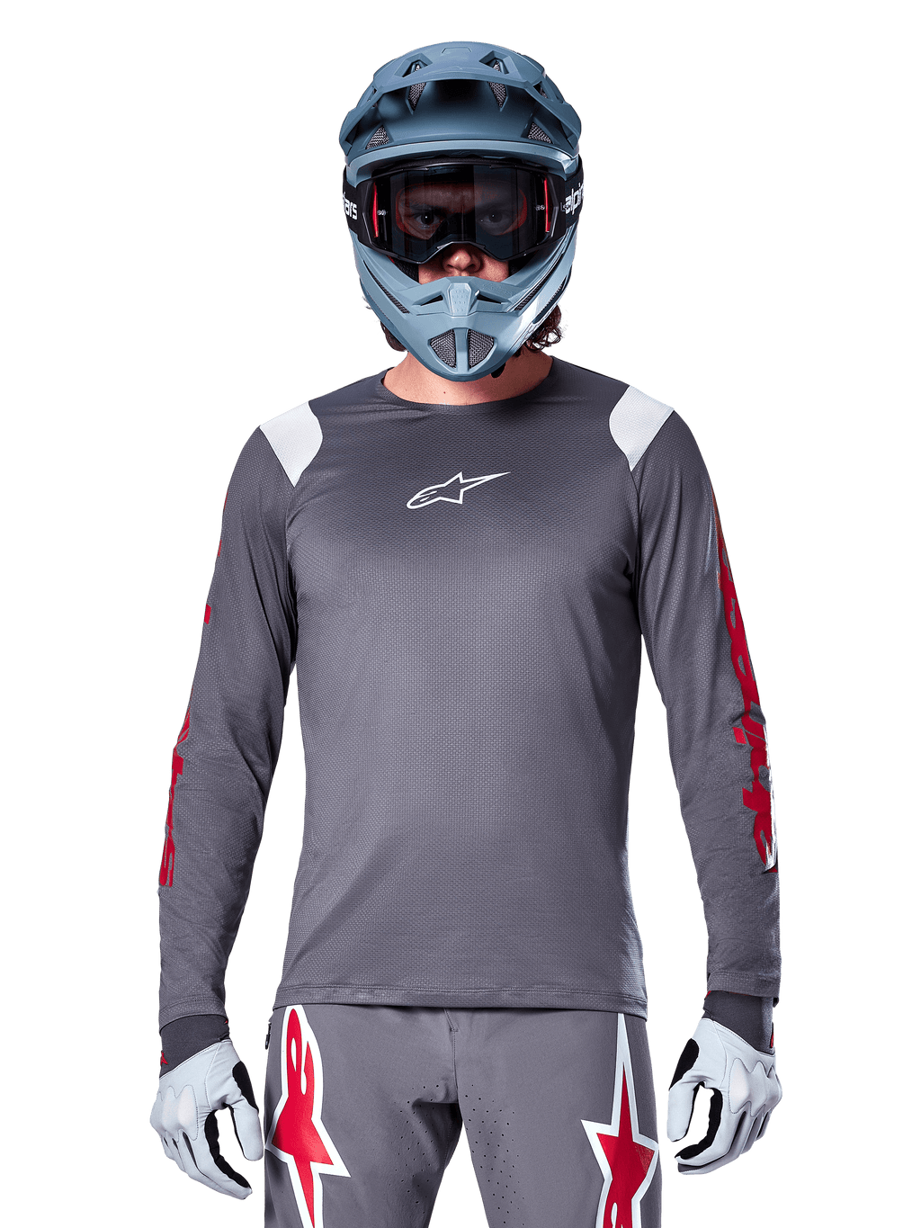 MTB rider wearing Alpinestars A-Supra Astar Long Sleeve Jersey, Dark Gray with red graphics on sleeves and white shoulder accents, matching gray pants with red star logos, blue full-face helmet and goggles, coordinated off-road cycling gear