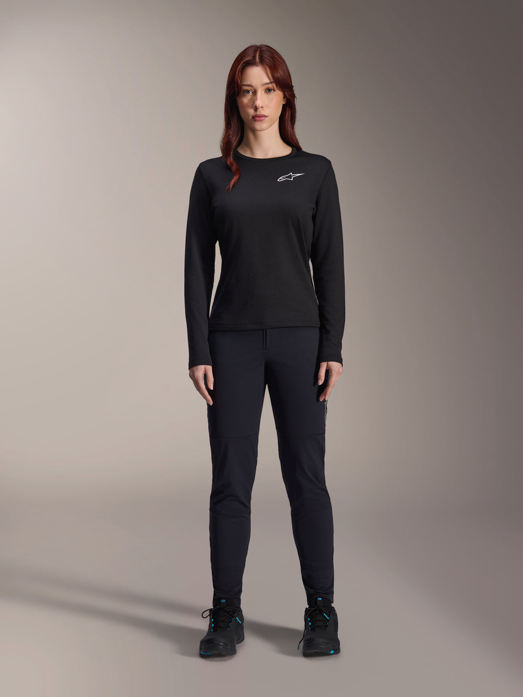 Alpinestars Stella A-Dura Thermo-Trikot, langärmeliges Damen-Mountainbike-Trikot in Schwarz, weißes Logo auf der Brust, kombiniert mit passender schwarzer Ausrüstung und Radschuhen, Studioporträt.