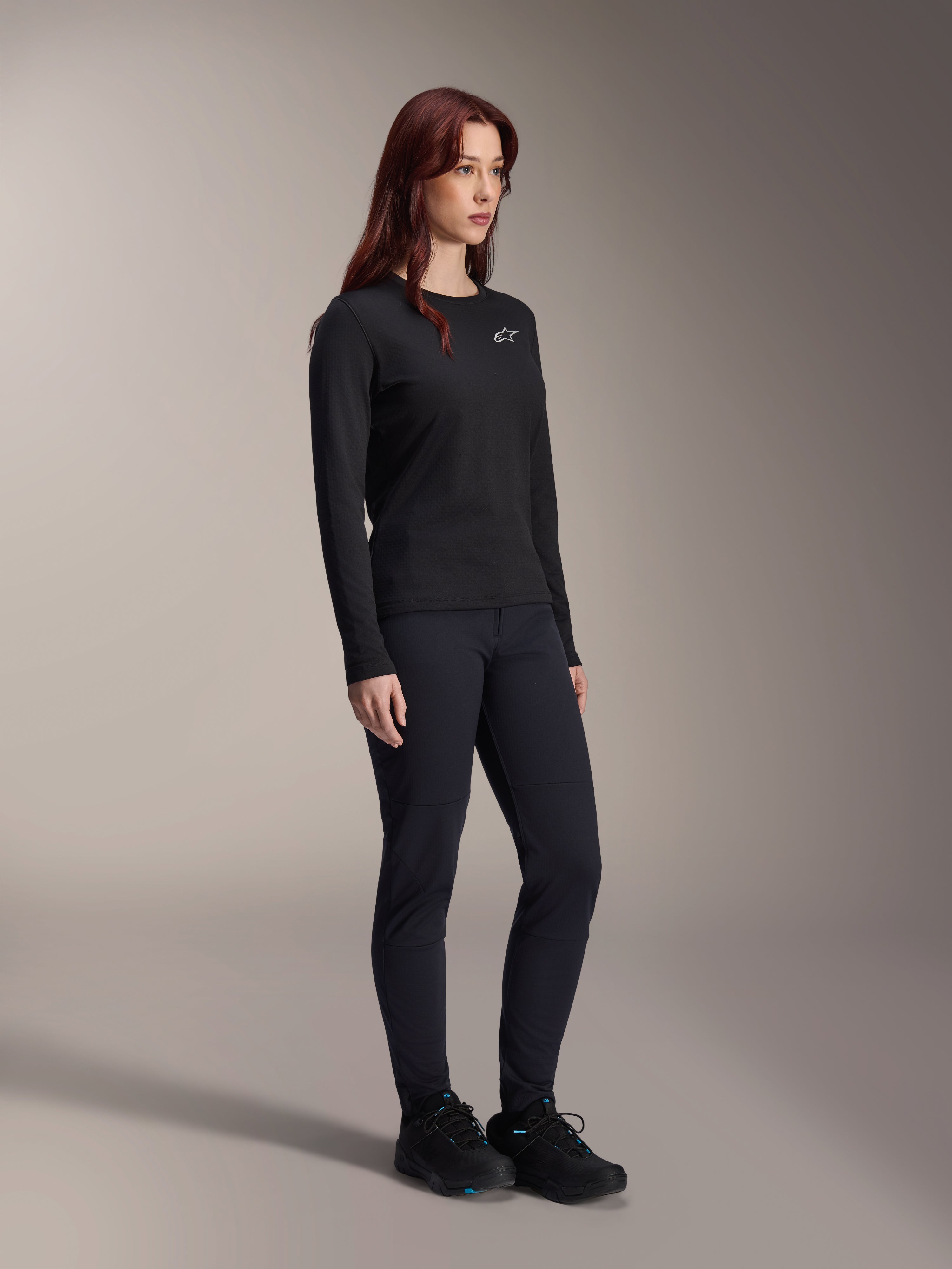 Alpinestars Stella A-Dura Thermo-Trikot für Damen, langärmeliges schwarzes MTB-Trikot mit weißem Logo auf der Brust, kombiniert mit passender schwarzer Hose und Sportschuhen, Studioaufnahme für leistungsstarke Fahrradbekleidung