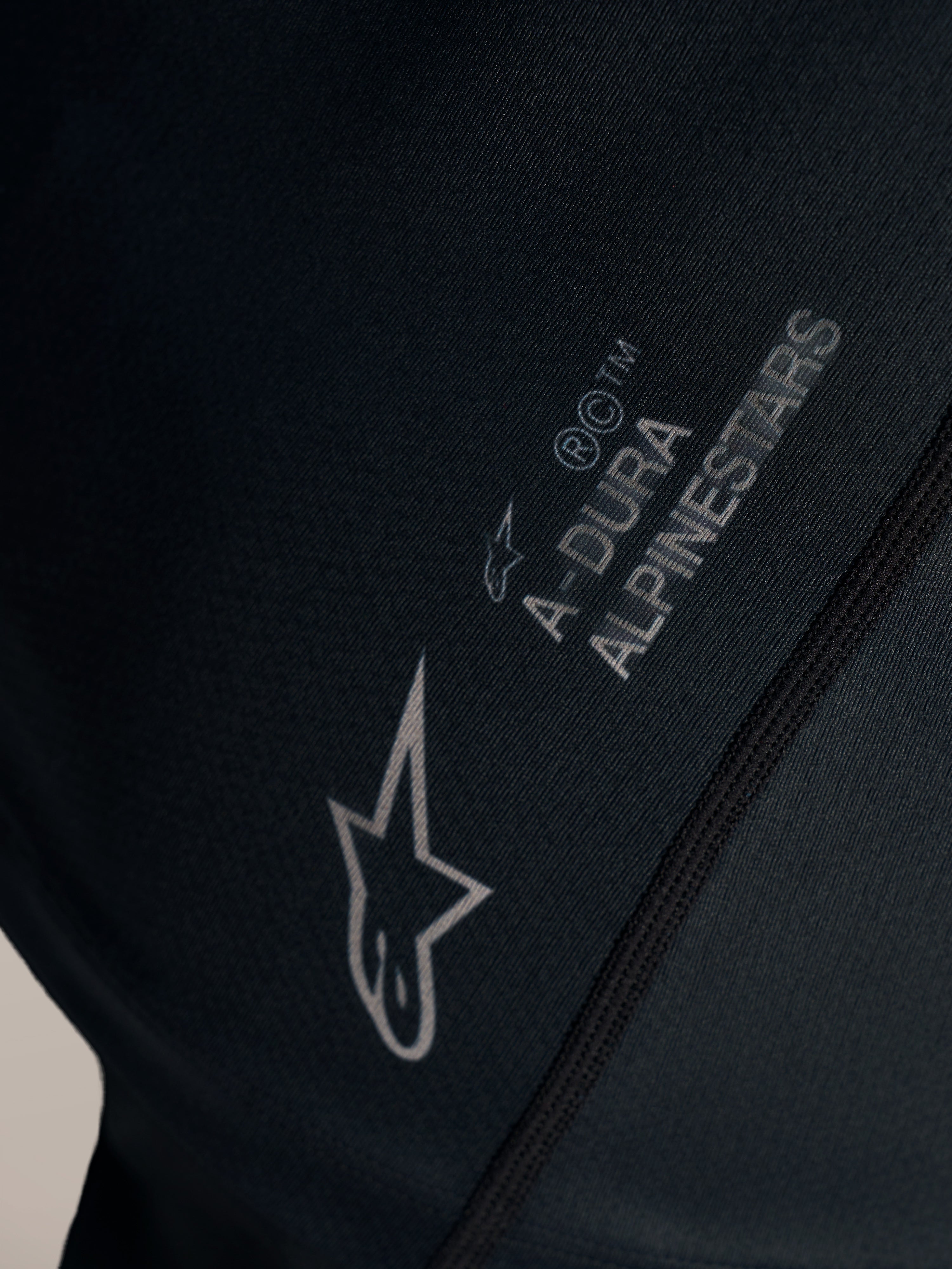 Schwarzes Stella A-Dura Ride Trikot, Detail des weißen Alpinestars-Logos und A-Dura Brandings auf Jacquard-Stoff.