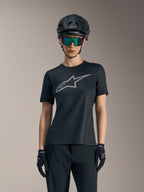 Schwarzes Stella A-Dura Ride Damen-Trikot mit grauem Brustlogo, kombiniert mit MTB-Helm, Goggles und Handschuhen.