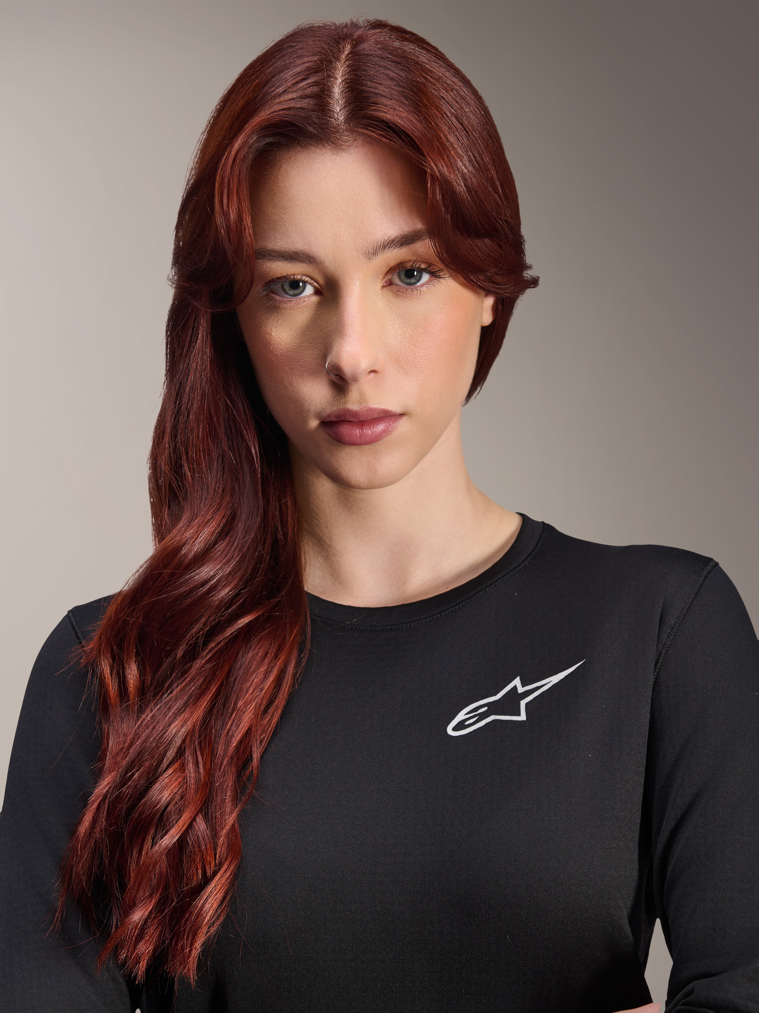 Alpinestars Stella A-Dura Thermal Jersey, Langarm-MTB-Trikot für Damen, Schwarz mit weißem A-Star-Logo auf der Brust, Nahaufnahme-Porträt einer Frau mit langen roten Haaren, Radbekleidung für kühles Wetter.
