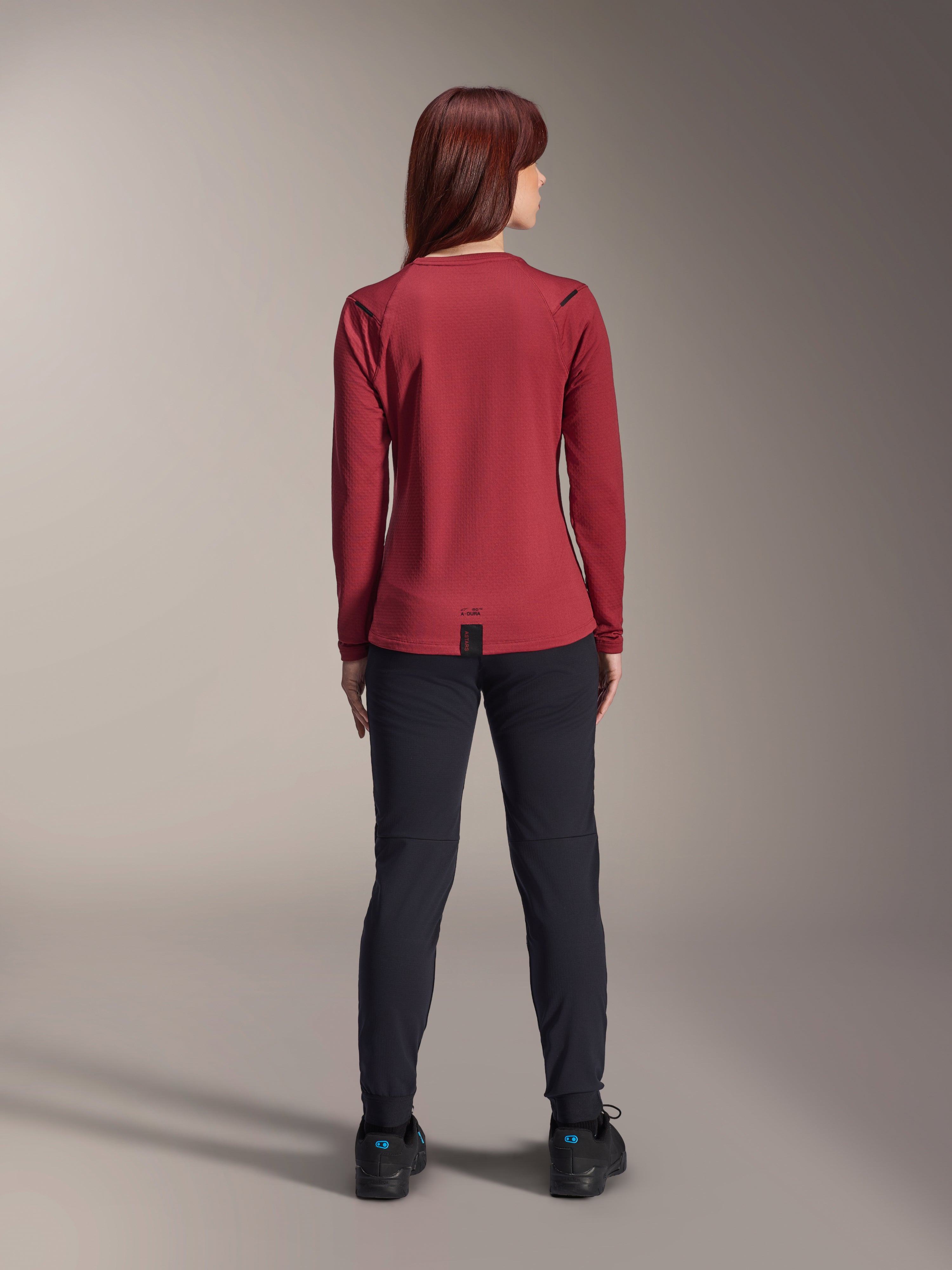 Alpinestars Stella A-Dura Thermohose, Mountainbike-Hose für Damen, Schwarz, getragen mit einem burgunderroten langärmeligen Thermo-Trikot, Rückansicht zeigt die technische Passform und Konstruktion für das Radfahren bei kaltem Wetter.