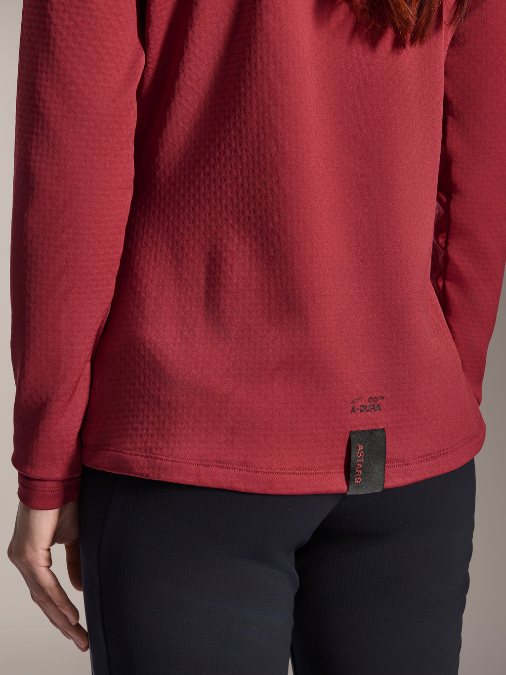 Alpinestars Damen Stella A-Dura Thermo-Trikot, Burgunderrot, Nahaufnahme des hinteren Saums mit A-Dura-Branding und gewebtem ASTARS-Etikett, strukturiertes isoliertes Fleece-Gewebe, Damen-Mountainbike-Bekleidung