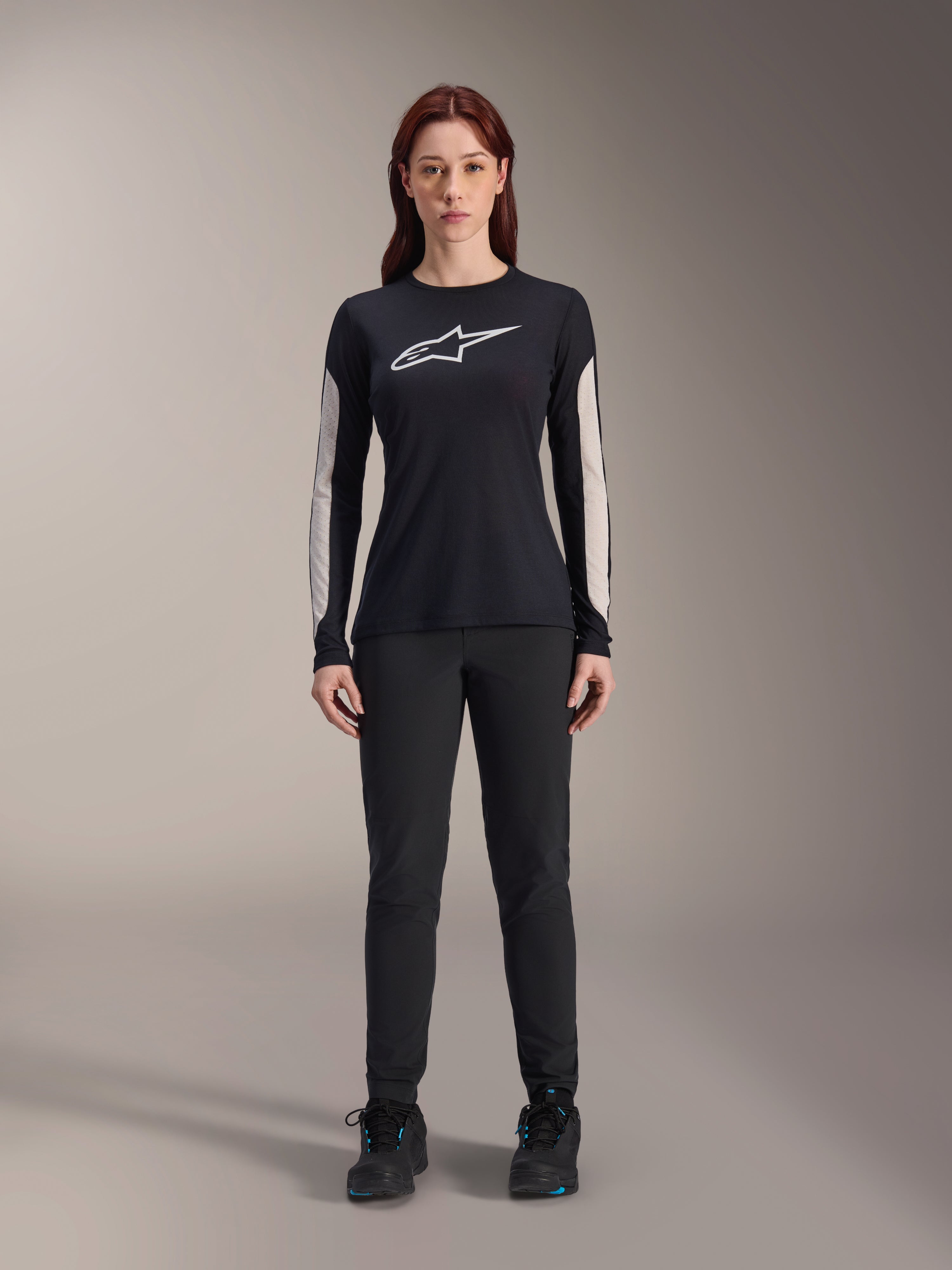 Frau im Alpinestars Stella A-Dura Dri Astar Langarmtrikot, Schwarz mit weißem Brustlogo und hellen Mesh-Ärmeleinsätzen, kombiniert mit schwarzer Hose und schwarzen Schuhen, technische Mountainbike-Bekleidung