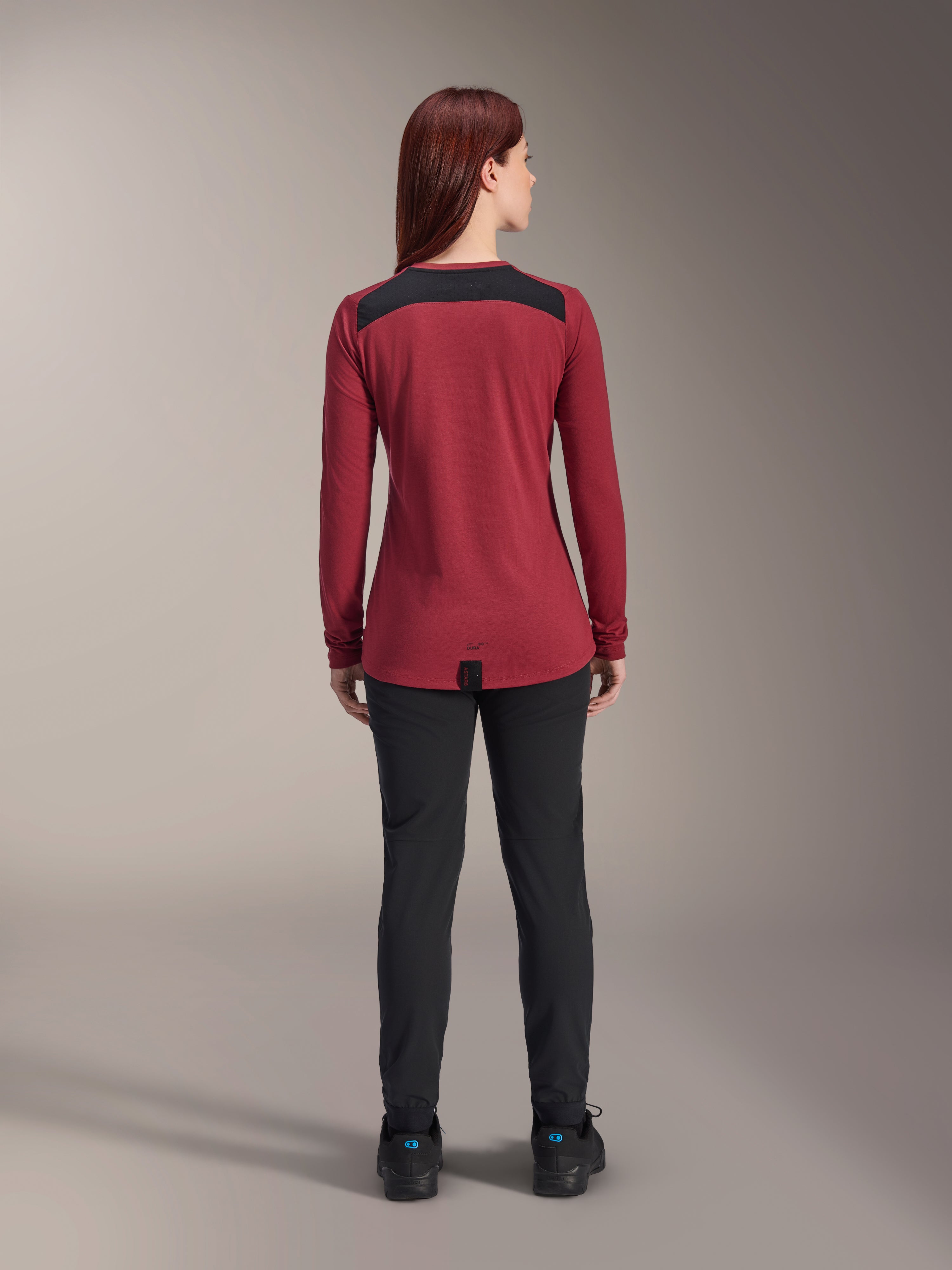 Alpinestars Stella A-Dura Dri Astar Langarmtrikot für Damen, Burgunderrot mit schwarzen Mesh-Schultereinsätzen, technische MTB-Bekleidung in der Rückansicht mit schwarzer Hose, verlängerter Rückensaum für optimale Abdeckung beim Radfahren