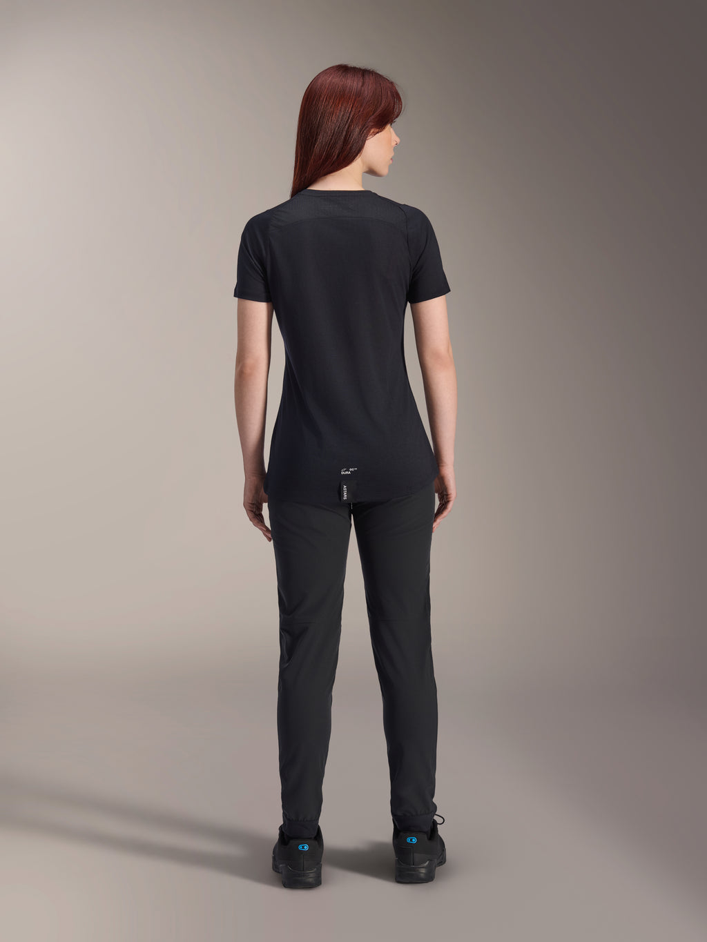 Alpinestars Damen Stella A-Dura Dri Switch Kurzarmtrikot, Schwarz, Rückansicht an einem Model, mit längerem abfallendem Saum und technischen Mesh-Einsätzen, kombiniert mit schwarzer Hose, Performance-MTB-Fahrradausrüstung