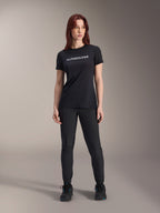 Alpinestars Stella A-Dura Dri Switch Kurzarmtrikot für Damen in Schwarz, weißes Logo-Branding auf der Brust, kombiniert mit schwarzer technischer Hose und schwarzen Sportschuhen, Ganzkörper-Studioaufnahme.