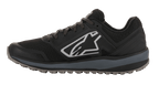 Alpinestars Meta Trail Schuhe, Performance-Laufschuh, Schwarz und Dunkelgrau, Seitenprofil mit großem weißen Astars-Logo, dunkelgraue Zwischensohle, profilierte ölbeständige Gummisohle, konzipiert für Komfort im Fahrerlager und Motorsport-Crews.