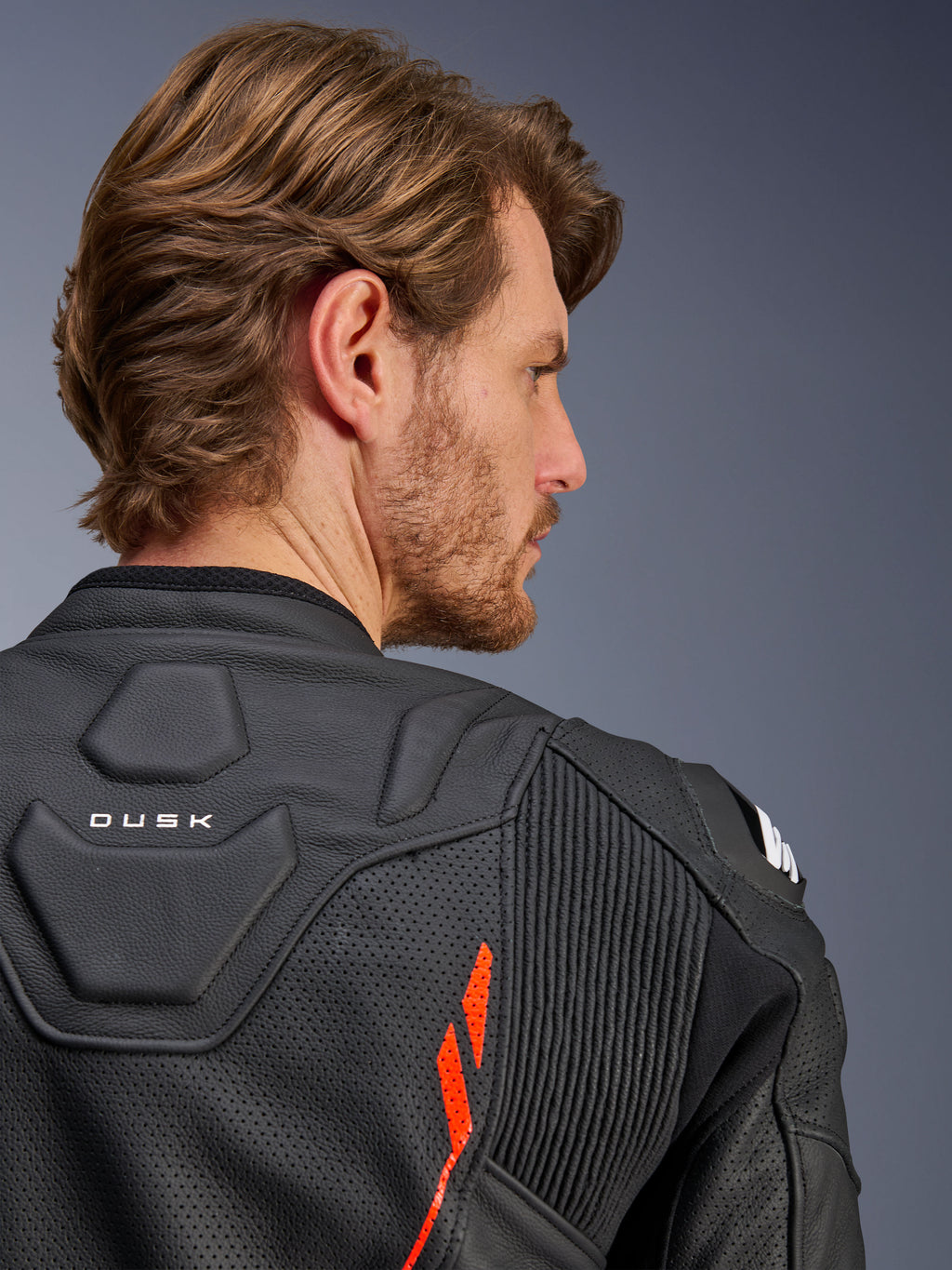 Alpinestars Dusk Airflow Leather Jacket, Black Red Fluo, close-up of the upper back and shoulder, featuring perforated leather for ventilation and accordion stretch panels, 'DUSK' branding detail, worn by a male model