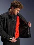 Alpinestars Ignite Air Jacke, schwarze Urban-Motorradjacke, mit leuchtend orangefarbenem, abnehmbarem winddichtem Futter und Mesh-Gewebe, Innenansicht mit wasserdichtem Fach, getragen mit schwarzem Alpinestars Logo-T-Shirt.
