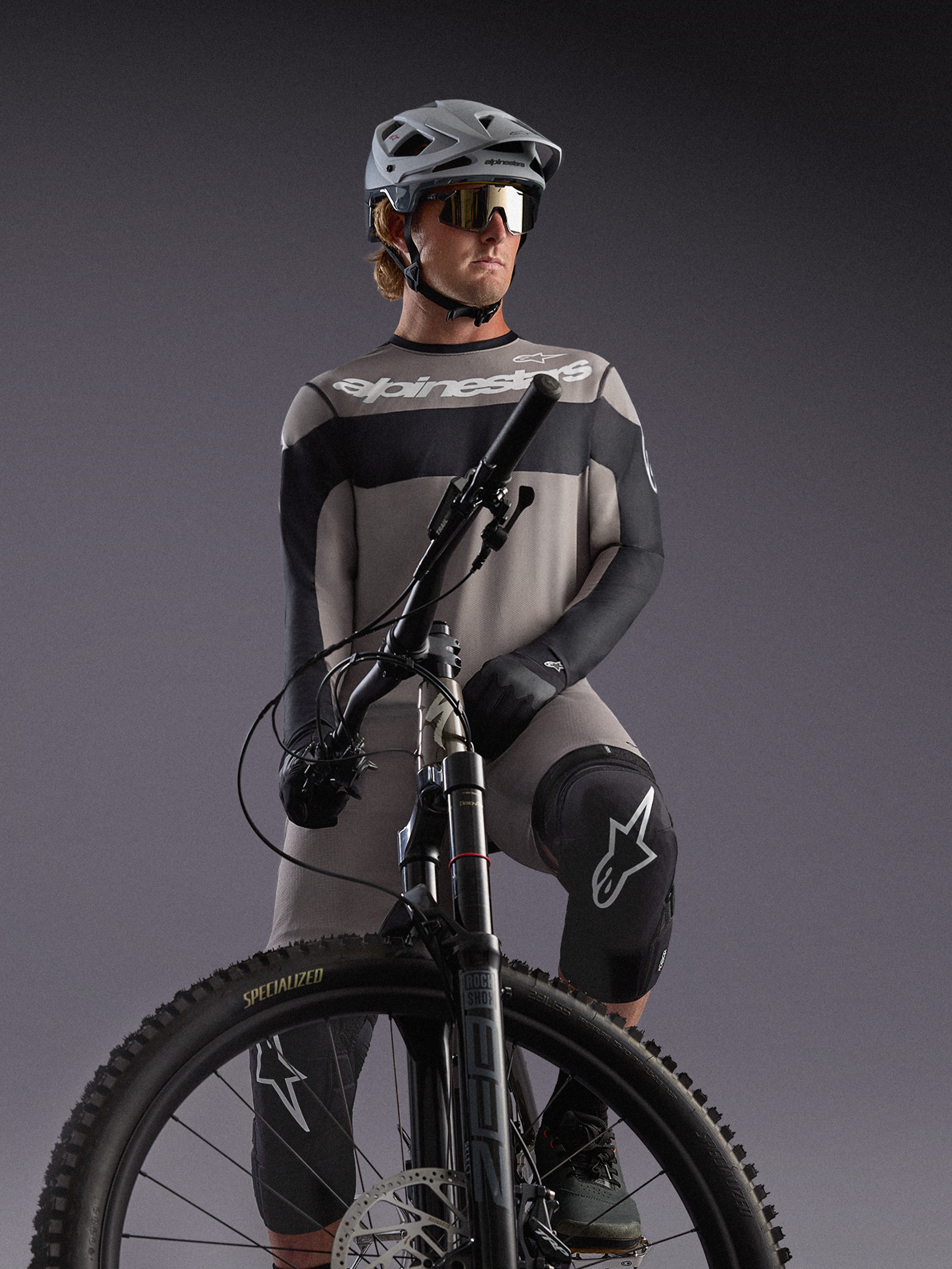 Graues Alpinestars A-Dura Race Langarmtrikot an einem MTB-Fahrer, mit schwarzen Akzenten und Profi-Radausrüstung.