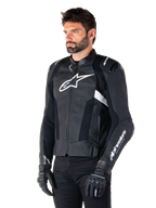 Alpinestars Missile V3 Lederjacke, Schwarz und Weiß, getragen von einem Mann mit schwarzen Motorradhandschuhen, mit einem markanten weißen Alpinestars-Logo auf der Brust, externen Schulter-Slidern und perforierten Einsätzen für einen rennsportinspirierten Look.