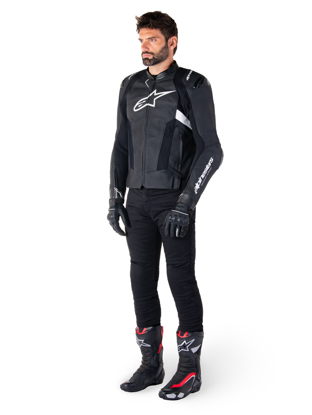 Männlicher Motorradfahrer in der Alpinestars Missile V3 Lederjacke in Schwarz und Weiß, mit einem weißen Brustlogo und perforierten Ledereinsätzen, kombiniert mit einer schwarzen Motorradhose, schwarzen Handschuhen und schwarz-roten Rennstiefeln für einen kompletten sportlichen Riding-Look.