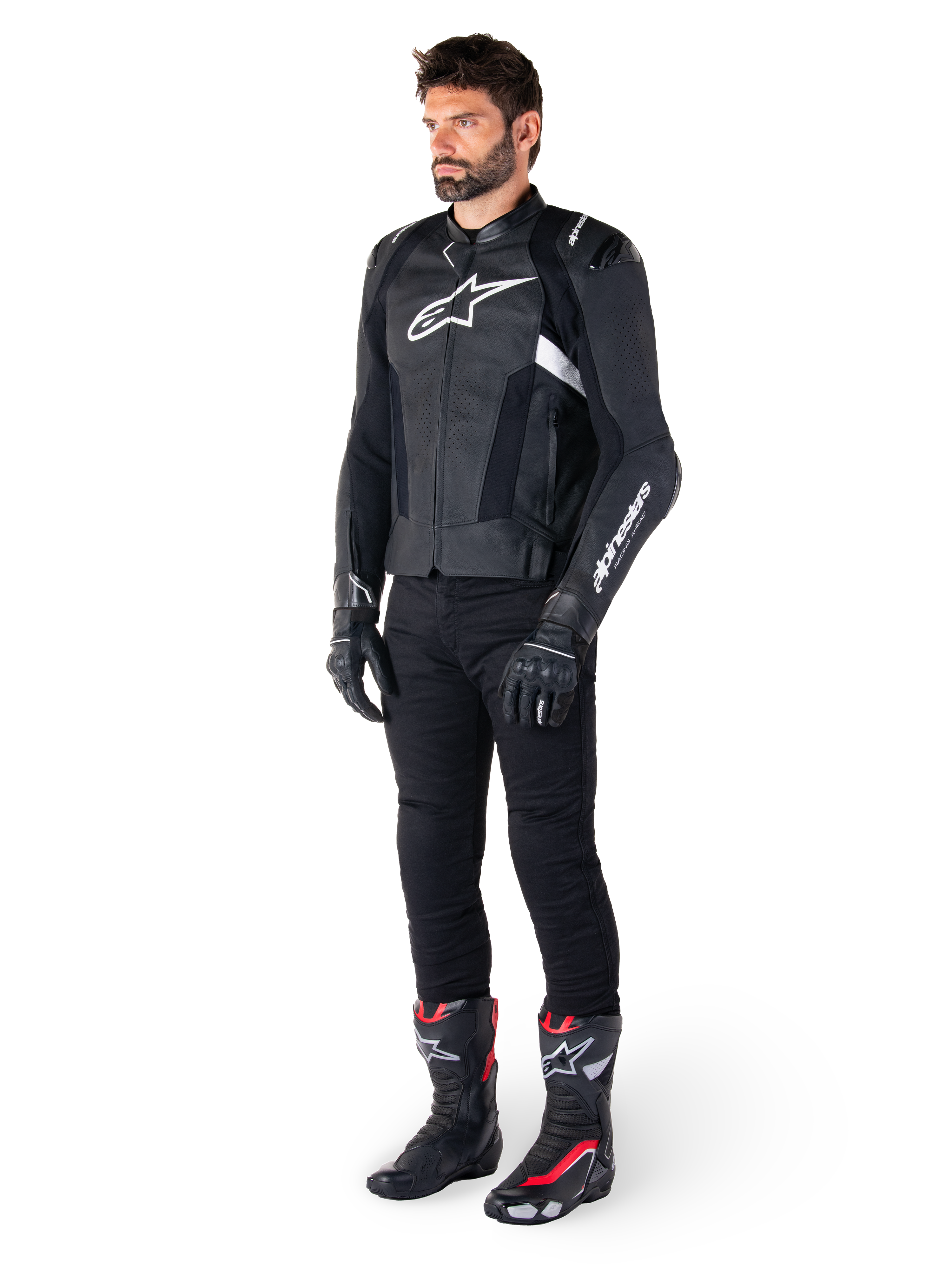 Männlicher Motorradfahrer in der Alpinestars Missile V3 Lederjacke in Schwarz und Weiß, mit einem weißen Brustlogo und perforierten Ledereinsätzen, kombiniert mit einer schwarzen Motorradhose, schwarzen Handschuhen und schwarz-roten Rennstiefeln für einen kompletten sportlichen Riding-Look.