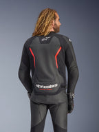 Alpinestars GP Force V2 Leather Jacket, Black and Red Fluo, back view on a model, featuring white Alpinestars logo and 'RACING AHEAD' text, paired with black leather motorcycle pants and gloves.