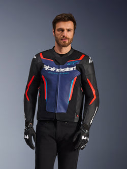Alpinestars GP Force V2 Leather Jacket, Black Blue and Red Fluo, worn by a male model with black gloves and pants, featuring a blue chest panel with 'Alpinestars Racing Ahead' text, red accents, and external shoulder shields, sport motorcycle protective gear