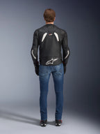 Rückansicht der Alpinestars GP Plus R V4 Rideknit Lederjacke, Schwarz und Weiß, mit einem großen weißen Logo im unteren Rückenbereich und Branding an den Ärmeln, getragen mit blauen Motorradjeans und schwarzen Stiefeln, zur Veranschaulichung der technischen Konstruktion und sportlichen Passform.
