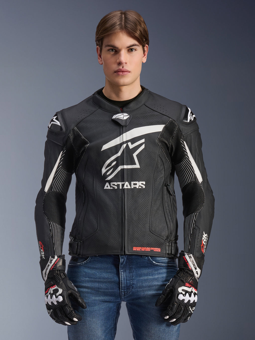 Alpinestars GP Plus R V4 Rideknit Lederjacke, Schwarz und Weiß, Motorrad-Rennjacke getragen von einem männlichen Model mit passenden Handschuhen und Jeans, markantes weißes ASTARS-Logo auf der Brust, perforierte Lederpaneele und schützende Schulterslider