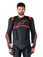Alpinestars Missile V3 Ignition Lederjacke, Motorrad-Rennjacke, Schwarz und Fluo-Rot, getragen mit passenden Rennhandschuhen und Lederhose, mit perforierter Belüftung und markantem Alpinestars-Branding, professionelle Rennausrüstung