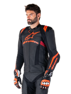 Alpinestars Missile V3 Ignition Lederjacke, Schwarz mit Akzenten in Red Fluo und Dark Red, getragen von einem männlichen Model mit passenden Rennhandschuhen und Lederhose, mit auffälligem Alpinestars-Branding, perforierten Ledereinsätzen und externen Schulterprotektoren, professionelle Motorrad-Rennausrüstung