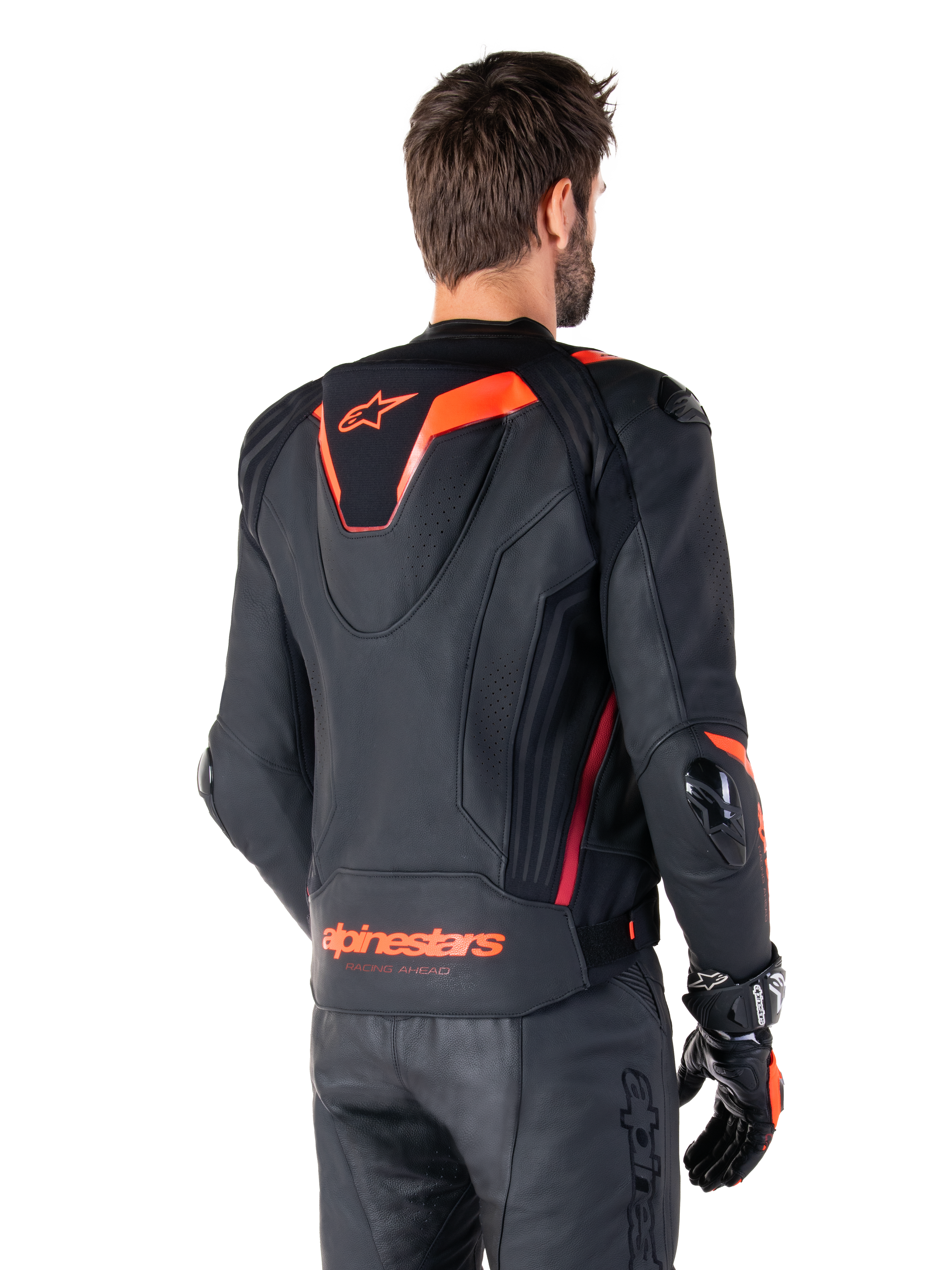 Alpinestars Missile V3 Ignition Lederjacke, Herren-Rennsportjacke, Schwarz mit Red Fluo Akzenten, Rückansicht mit schmalem aerodynamischem Sport-Höcker und Alpinestars-Logo am unteren Rücken, getragen mit schwarzer Lederhose und Rennsport-Handschuhen, schlankes professionelles Motorsport-Design