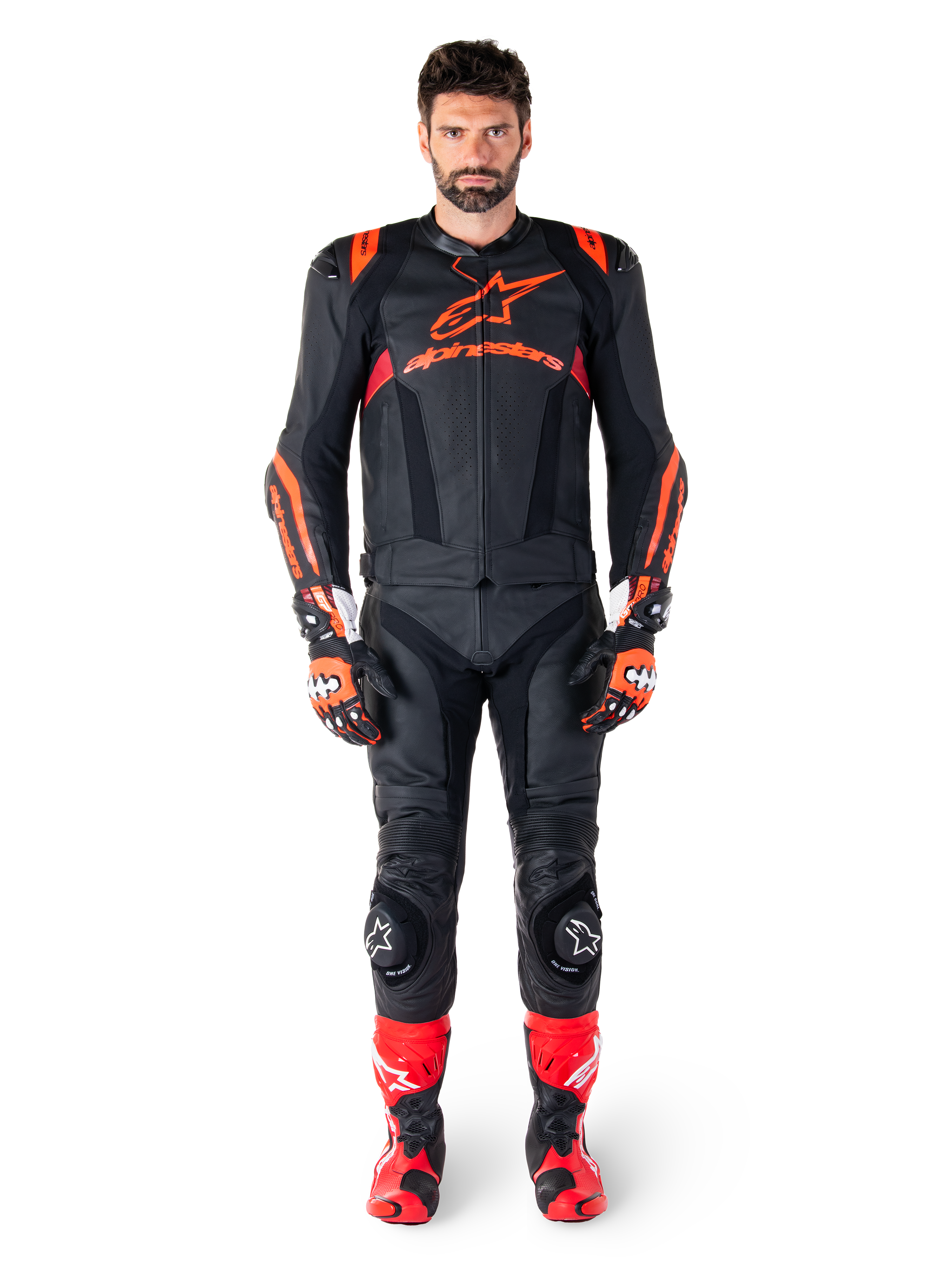 Männliches Model in der Alpinestars Missile V3 Ignition Lederjacke in Schwarz, Fluo-Rot und Dunkelrot, komplette Motorrad-Rennausrüstung mit passender Lederhose, Rennhandschuhen und Stiefeln, markantes Alpinestars-Branding auf der Brust, nach vorne gerichtete Pose, professionelles Sport-Fahrer-Outfit