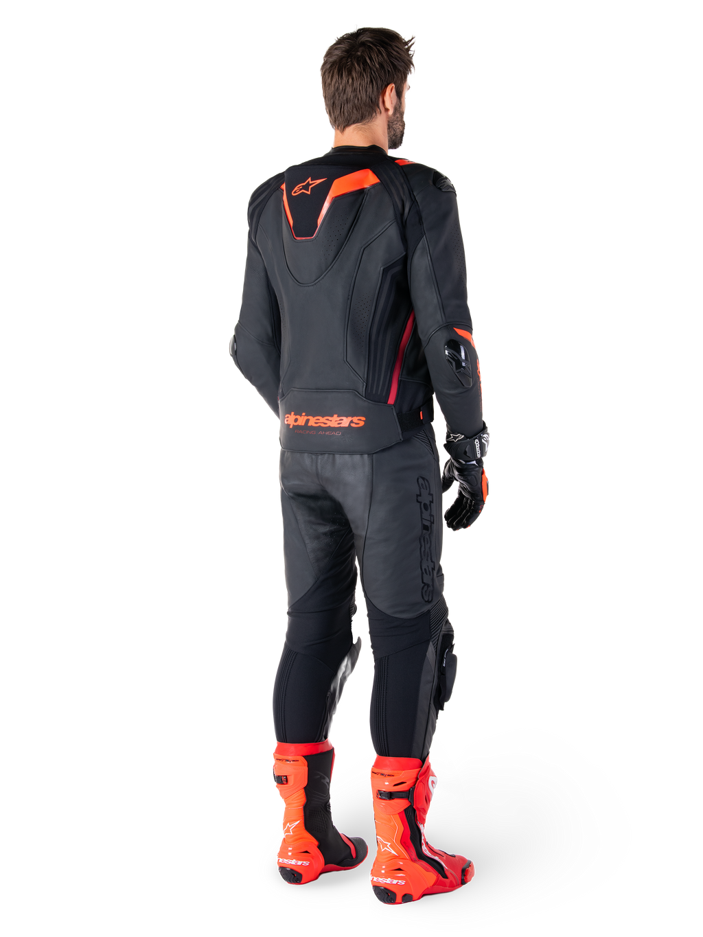 Alpinestars Missile V3 Ignition Lederjacke, Rennsport-Motorradjacke, Schwarz und Rot Fluo, Rückansicht eines Fahrers in vollständiger Rennbekleidung mit passender Lederhose, Handschuhen und roten Stiefeln, mit sportlichem Aero-Höcker und markantem Branding am unteren Rücken.